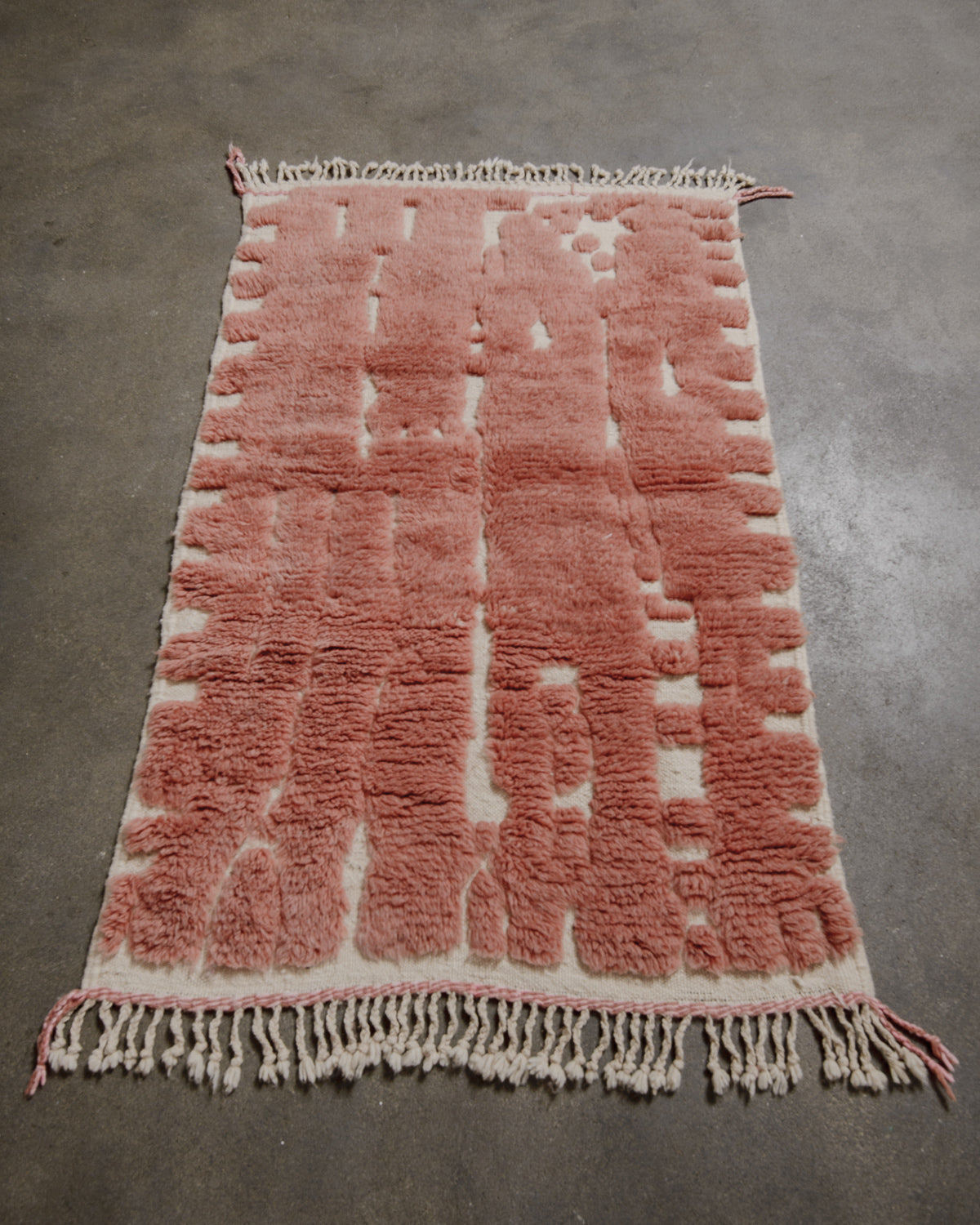 Rose coloured textured rug with cream accents on a gray concrete floor